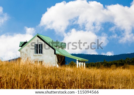 Country house in the American Southwest with tall golden grass and hills, blue sky and white puffy clouds.