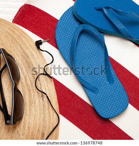 Flip flops, hat, towel, sunglasses and earphones for a day at the beach, spa or pool. Red, white and blue theme. Square format. Top view, looking down.