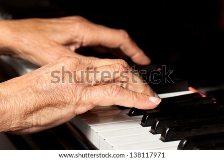 Old person's hands playing the piano. Close up view of skin texture and piano keys.