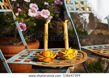 Lighted candles in a romantic night garden patio setting. Vintage blue French metal chairs and pink roses.