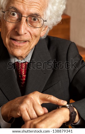 Impatient older man wearing a suit points at his watch and looks upset. Concept for lateness or time running out.