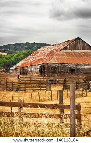 California landscape with with golden rolling hills and native oak trees and an old barn and fences. Location: Napa and Sonoma wine country region of northern California.