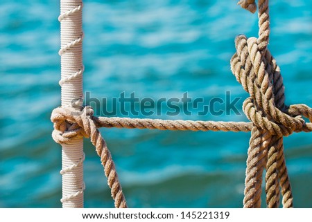 Close up detail of knotted ropes on a tall ship schooner under sail with blue water in the background
