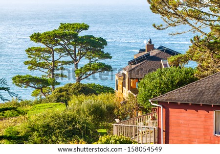 California houses on a hillside with views of the Pacific Ocean. One has solar panels installed on the roof. Location: Muir Beach, near San Francisco.