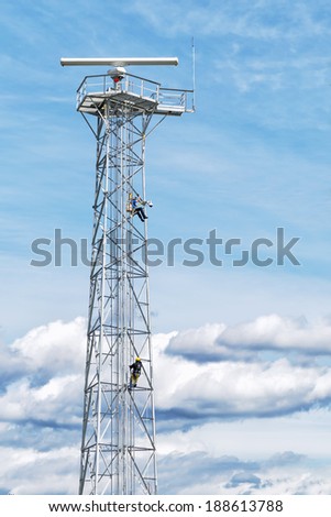 Radar tower with workers high up in the scaffolding, against a background of blue sky and clouds. Copy space for text.