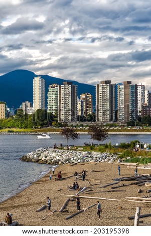 Popular dog beach in Vancouver, Canada, with dogs and people playing on the sand. Vancouver skyline of tall buildings in the background.
