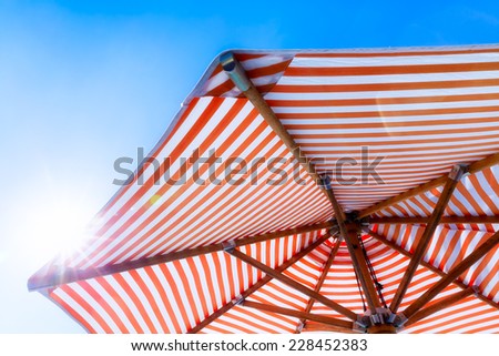 Orange and white striped beach umbrella with blue sky and natural sun flare. Copy space