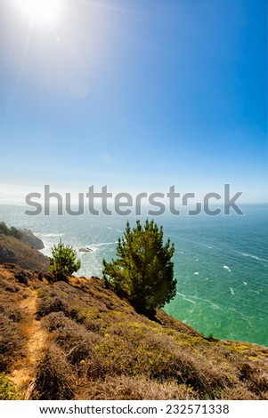 California coastal trail on a cliff overlooking the Pacific Ocean. Natural sun flare in a blue sky. Location: About 30 miles north of San Francisco. Copy space.