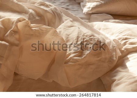 Rumpled unmade bed with linen duvet, sheets and pillows. Selective focus with shallow depth of field.  Background concept for romance.