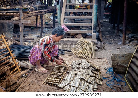 CAMBODIA-JAN 27, 2015: A woman working in a fish smoking business, the principal industry in this rural village on the Mekong River. She squats on the ground and makes a pile of the preserved fish.