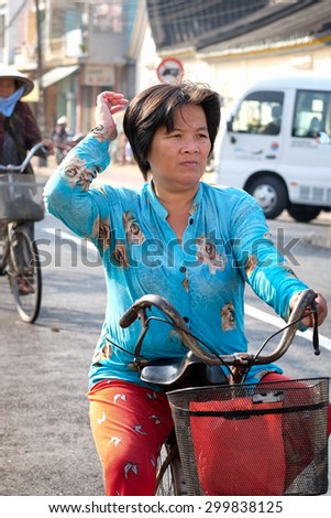 VIETNAM-JAN 23, 2015: Woman in a blue shirt and red pants riding a bicycle in the Mekong River port town of Sa Dec, known for its busy waterfront market and many commercial flower growers. Close up.