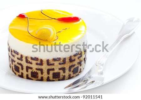 Lemon mousse individual cake on white plate with a sterling silver fork. Closeup isolated on white. Special occasion dessert.