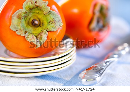 Fresh persimmons on a blue and white cloth with a silver knife and antique china plates