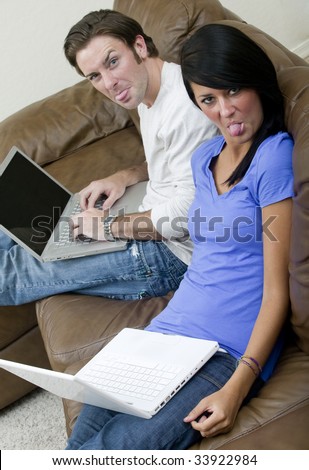 A young couple goof around while working on their computers on the couch