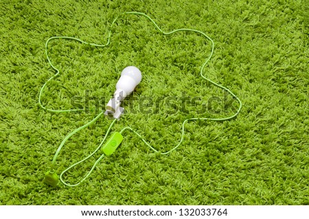 Wire flower plugged  to the earth. Energy saving lamp in the socket, with green wire, on the green carpet.