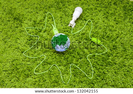 Pumping energy from the world. Made of threads ball connected with lamp in the holder, by green wire, on the green carpet.