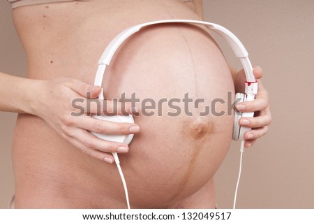 Pregnant woman give unborn child listen a music by headphones.