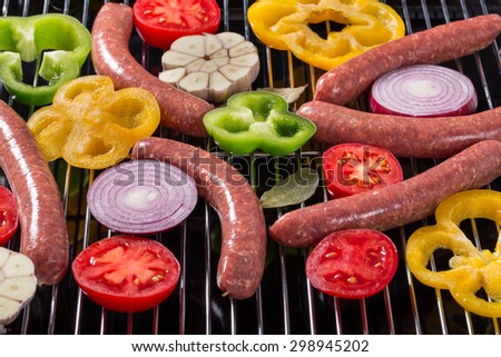homemade raw sausages on the grill with garlic, tomatoes, peppers and onions, a side view