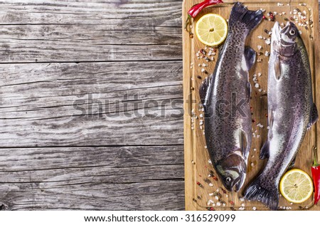 two raw trouts fishes with lemon slices, hot peppers and salt on the cutting board, rustic style, horizontal, top view