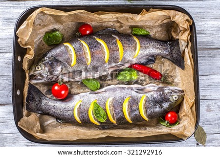 delicious raw trout fishes prepared for baking with potatoes, broccoli, lemon, tomatoes and spices in baking dish on a wooden background, top view, horizontal
