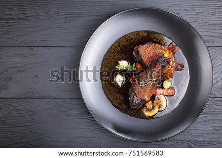 portion of tasty chicken stew - thigh and drumstick braised with wine, herbs, mushrooms and vegetables served on black plate on wooden table, festive Burgundian dish - Coq Au Vin, view from above Imagine de stoc © 
