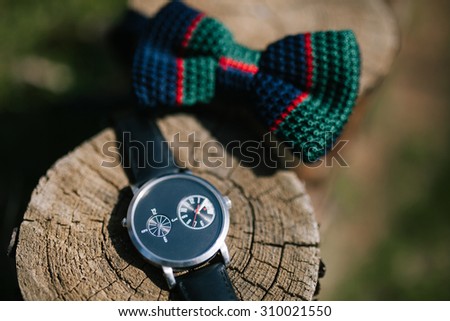 Stylish black watch and the blue and green wedding bowtie lying on the pine saw cut