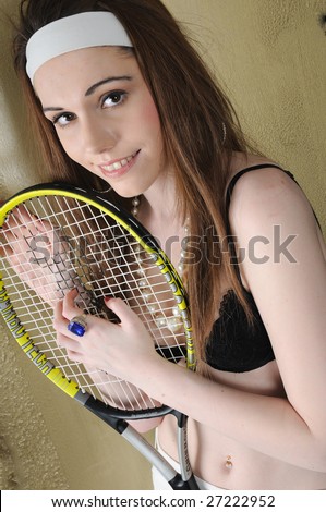 female fashion model holding on to the strings of a tennis racket wearing a white head band and wearing a black bra