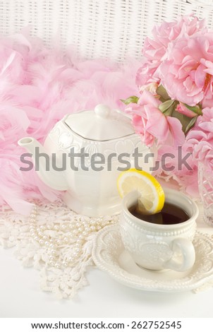 A vintage feminine tea party still life, with a teapot set, hot tea with lemon and fresh cut pink roses, perfect for Mothers Day, Easter or special occasion