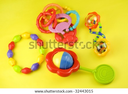 Colorful baby rattles and teething rings on a yellow background with copy space