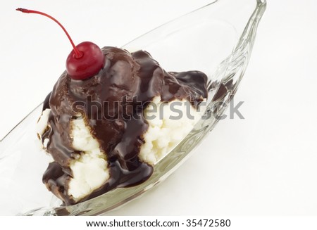 A vanilla ice-cream sundae with fudge topping and a cherry on top in a glass dish, isolated on white, diagonal with copy space