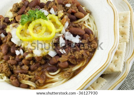 A bowl of homemade chili spaghetti, topped with cheese, chopped onion, and banana peppers,  horizontal macro