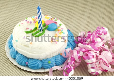 A one year birthday cake with one unlit candle, party ribbon on a textured background, horizontal with copy space