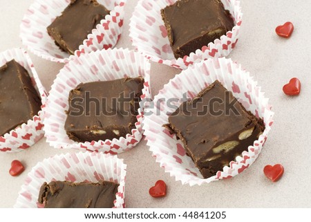 Homemade chocolate pecan fudge in Valentine paper candy holders with candy hearts, selective focus,horizontal
