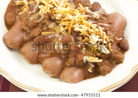 A plate of chili dogs topped with grated cheese, horizontal closeup