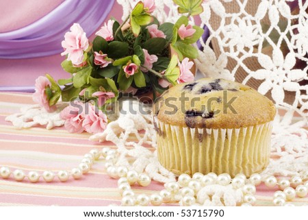 A delicious fresh blueberry muffin with a vintage background, lace, pearls and pink flowers