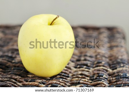 A yellow apple on a brown woven basket service with shallow depth of field and copy space