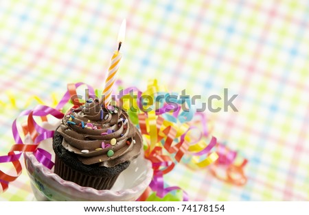 A delicious chocolate cupcake with one lit candle and colorful party ribbons