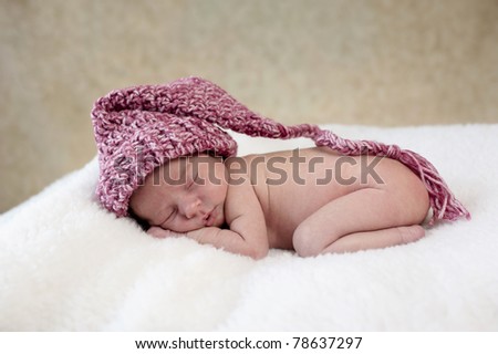 A studio portrait of a beautiful one week old baby girl sleeping, wearing a hat