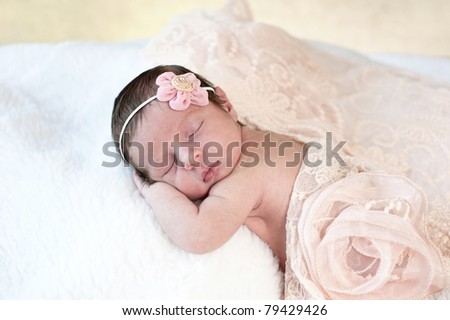 A beautiful sleeping newborn baby girl with a peach colored vintage lace scarf and flower headpiece