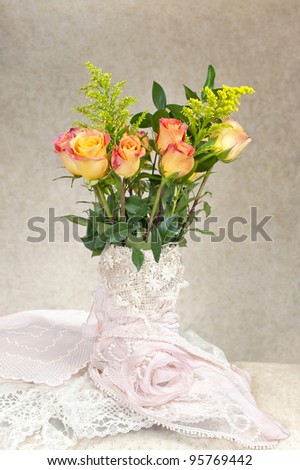 A vase covered with antique lace filled with a bouquet of long stemmed rainbow roses, plenty of copy space for text