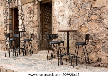 high bar stools and tables in the front of a rustic restaurant building in Mexico