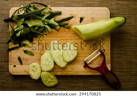 Concept of preparing a vegan meal, cut and peeled cucumber on a wooden cutting board