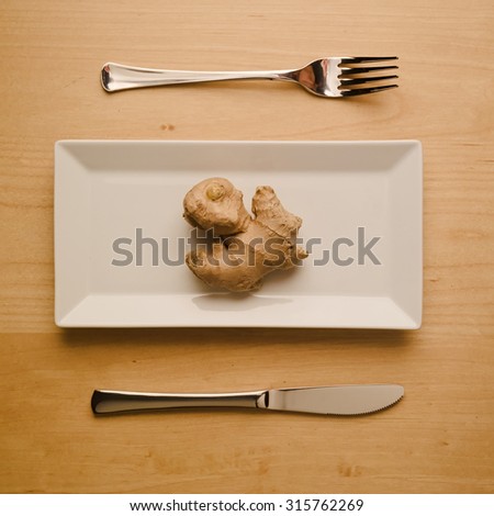 Concept of vegan and vegetarian low-carb diet. A single raw and uncut ginger root on a square rectangle plate with table knife and fork. Top down view.