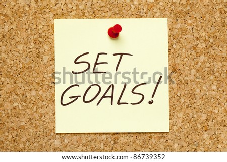 SET GOALS! written on an yellow sticky note on an office cork bulletin board.
