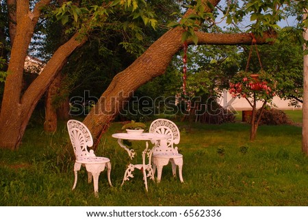a warmly lit yard with iron chair and table and hanging flowers