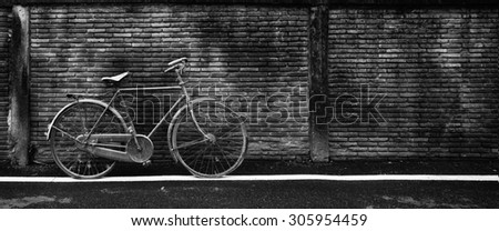 Old rusty bicycle against an old wet brick wall, black and white