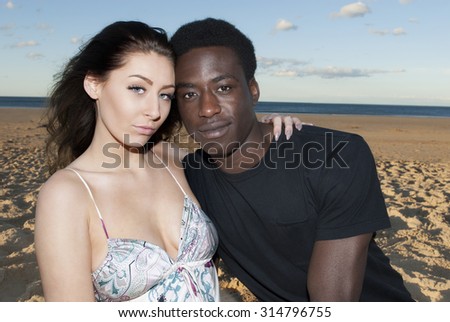 Young couple multicultural head and shoulders heads together looking serious on beach  romantic  emotions