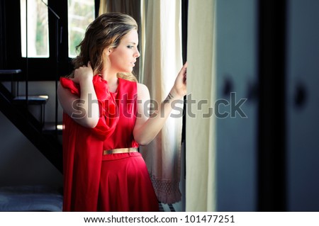 Portrait of a beautiful blonde woman in window wearing a red dress
