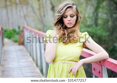 Beautiful blonde girl, dressed with a beige dress, standing in a rural bridge, with eyes closed