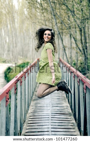 Beautiful blonde girl, dressed with a beige dress, jumping in a rural bridge